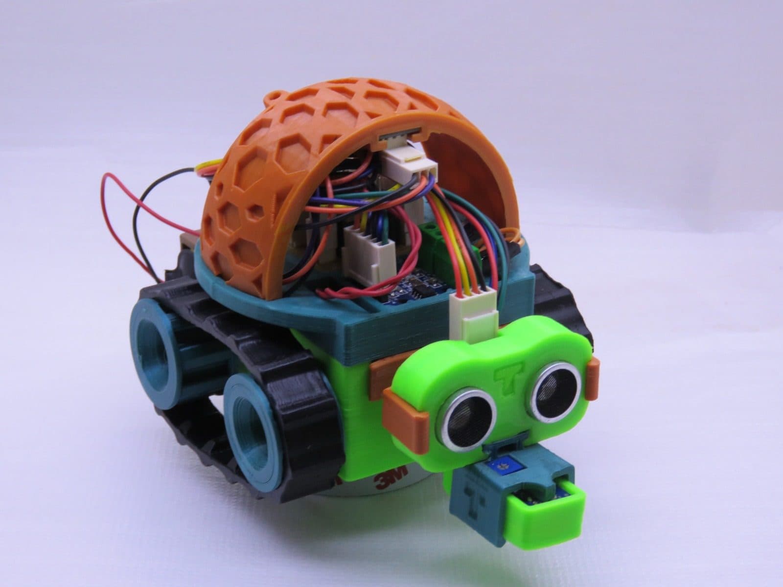 Robô TurTle-T montado: cúpula laranja vazada impressa em 3D, esteiras pretas e cabeça verde com dois sensores ultrassônicos.
