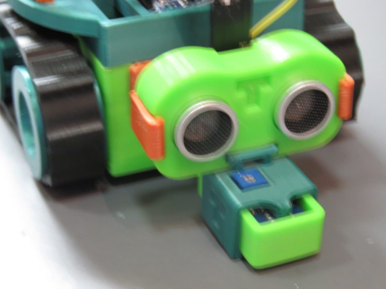 Close da cabeça do TurTle-T: sensor ultrassônico em suporte verde impresso, com presilhas laranja e sensor infravermelho abaixo.